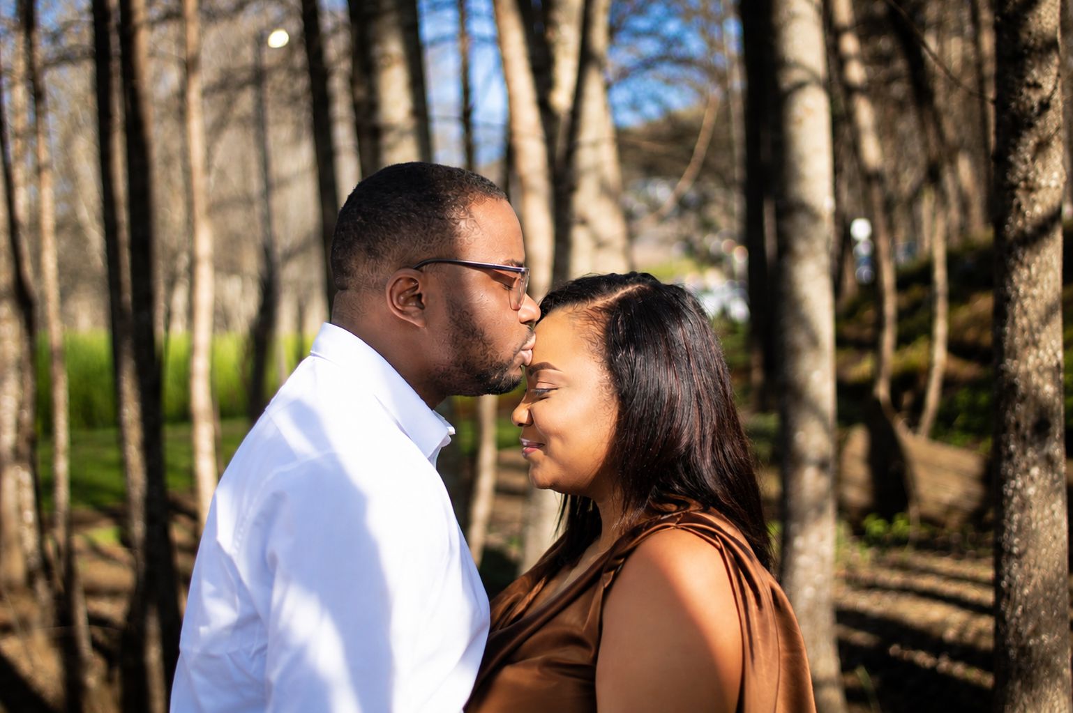 A tender forehead kiss between the couple in the woods